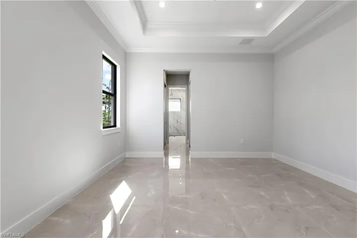 Empty room with a raised ceiling, ornamental molding, light marble finish flooring, and recessed lighting
