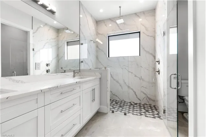 Bathroom featuring healthy amount of natural light, double vanity, a marble finish shower, light marble finish floors, and recessed lighting