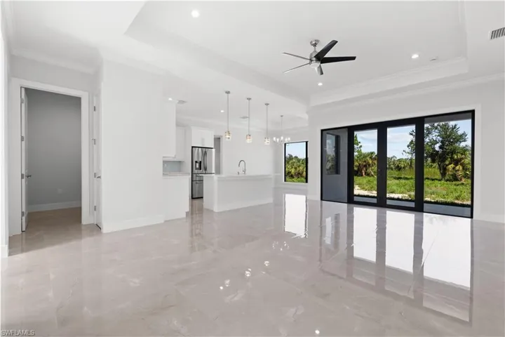 Unfurnished living room with a tray ceiling, ornamental molding, light marble finish floors, recessed lighting, and ceiling fan