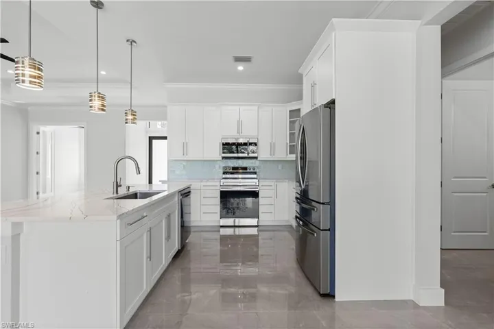 Kitchen with crown molding, a center island with sink, stainless steel appliances, tasteful backsplash, and white cabinets