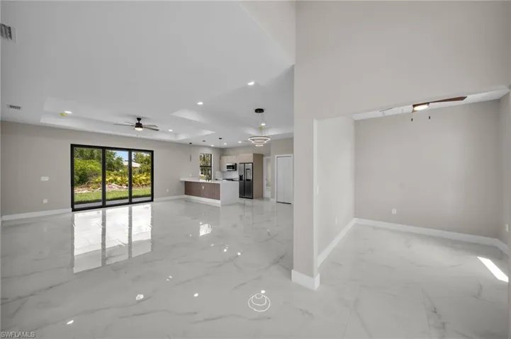 Unfurnished living room featuring a ceiling fan, a tray ceiling, light marble finish floors, and recessed lighting
