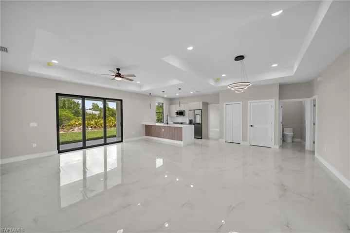 Unfurnished living room with a tray ceiling, light marble finish flooring, recessed lighting, and ceiling fan