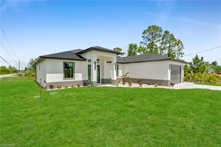 Prairie-style home featuring concrete driveway, a shingled roof, stucco siding, and a front lawn