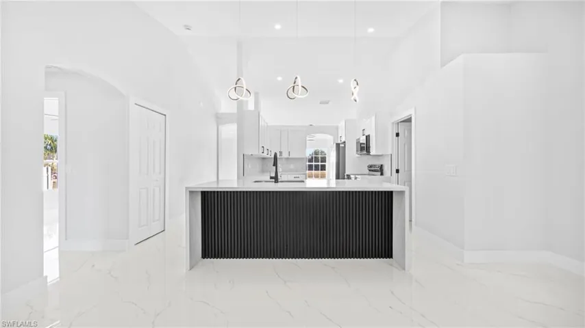 Kitchen featuring white cabinets, arched walkways, light stone counters, light marble finish flooring, and high vaulted ceiling