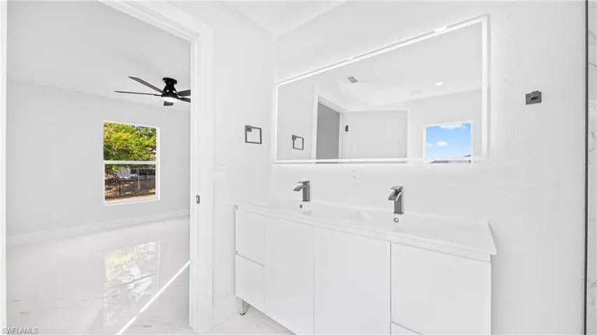 Full bath featuring double vanity, light marble finish flooring, and ceiling fan
