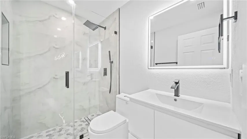 Bathroom with a textured wall, vanity, and a marble finish shower