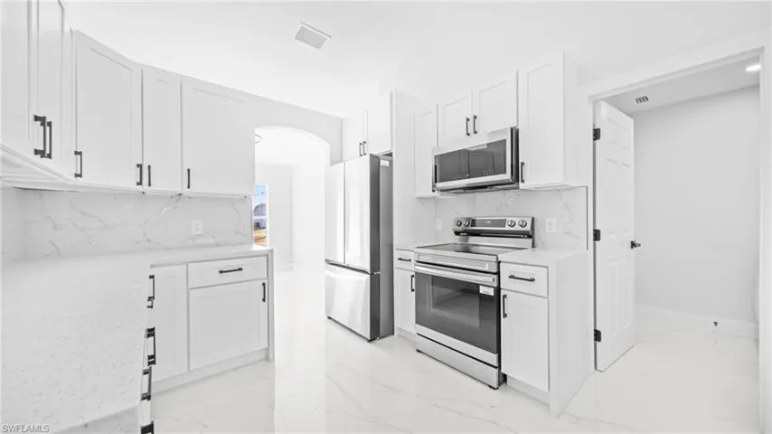 Kitchen featuring appliances with stainless steel finishes, white cabinets, light stone countertops, and arched walkways