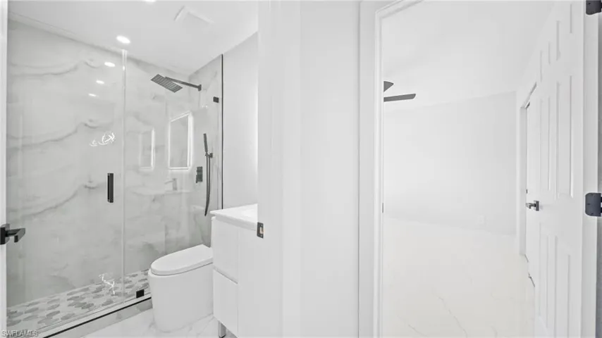Full bathroom with vanity, a marble finish shower, light marble finish flooring, and recessed lighting