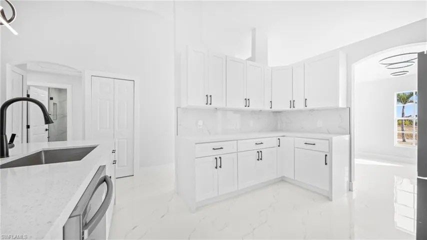 Kitchen featuring arched walkways, white cabinetry, and light stone counters