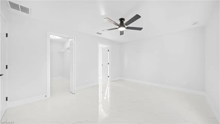 Unfurnished bedroom with a walk in closet, ceiling fan, and light marble finish flooring