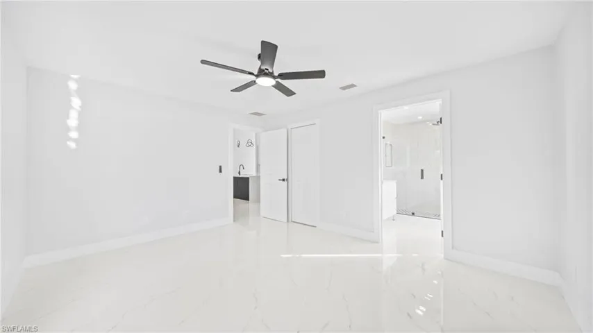 Unfurnished bedroom featuring ceiling fan, light marble finish flooring, a closet, and ensuite bathroom