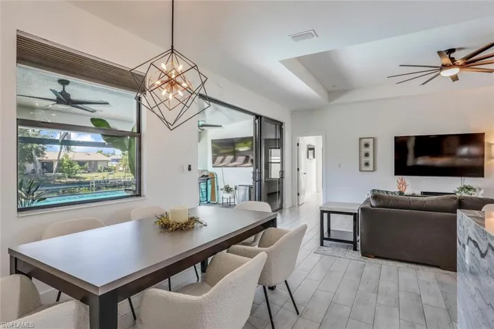 Open-concept dining and living area featuring large windows, a geometric chandelier, and wood tile like flooring