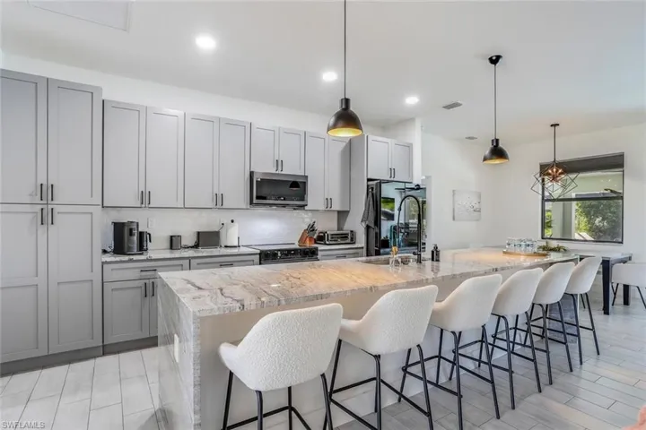 Kitchen featuring a large island with granite waterfall, pendant lighting, motion active undercabinet lighting, Samsung appliances with smart refrigerator.