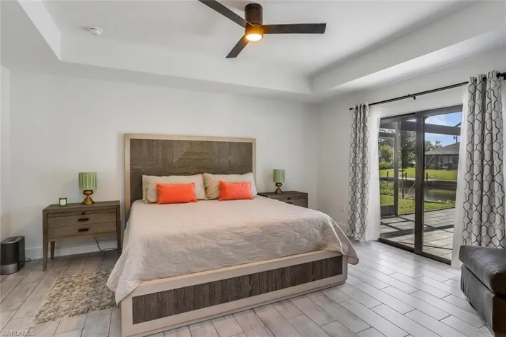 Primary Bedroom featuring tray ceiling, wood-finish flooring, and a ceiling fan with direct access to pool lanai.