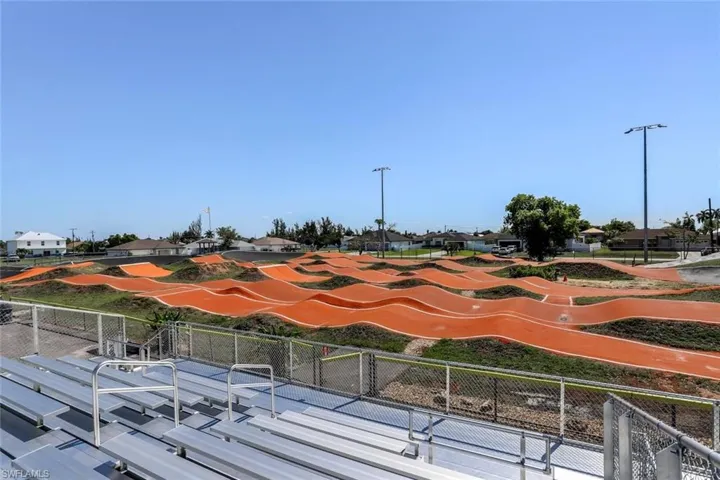 Expansive outdoor BMX Sports track with multiple orange-surfaced ramps and green-lined mounds