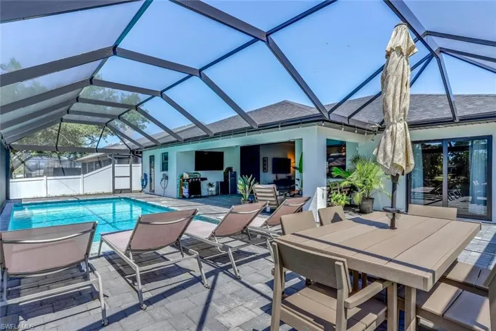 Screened-in outdoor living space featuring a rectangular swimming pool, paver patio, full enclosure, and exterior lighting