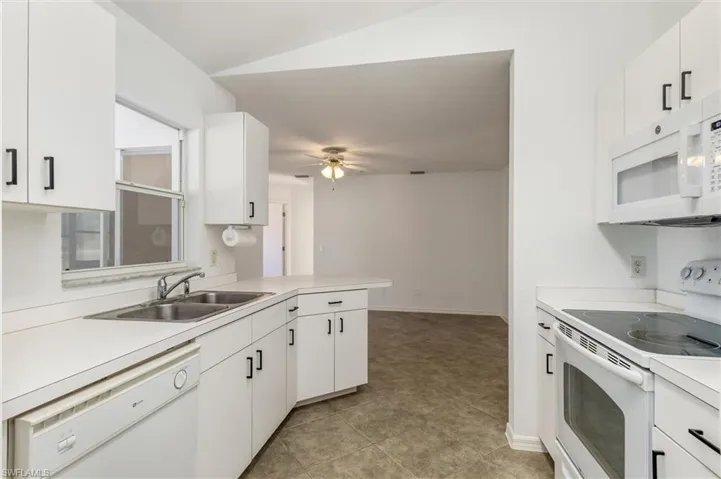 Kitchen featuring white cabinetry with black hardware, white countertops, dual basin stainless steel sink, and white appliances