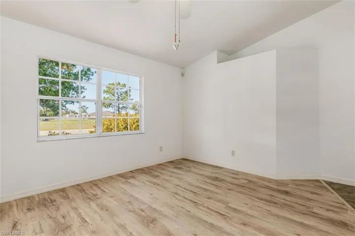 Room featuring a large grid-pane window, wood-finish flooring, and white painted walls