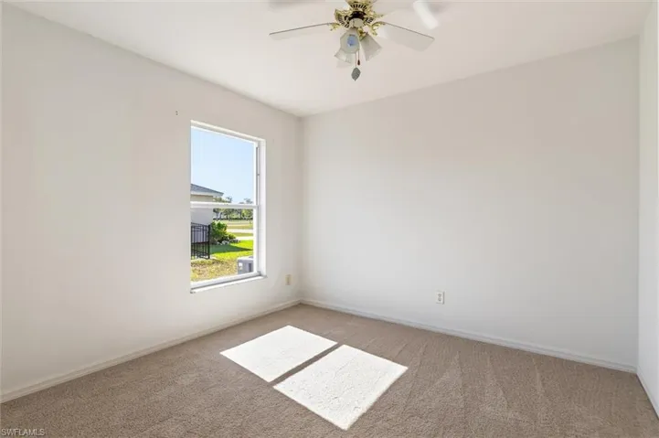 Bright interior space featuring a single window, overhead ceiling fan, and light-toned carpet flooring
