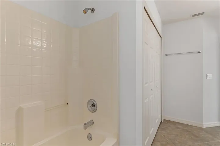 Bathtub with integrated shower, chrome fixtures, and a tiled surround