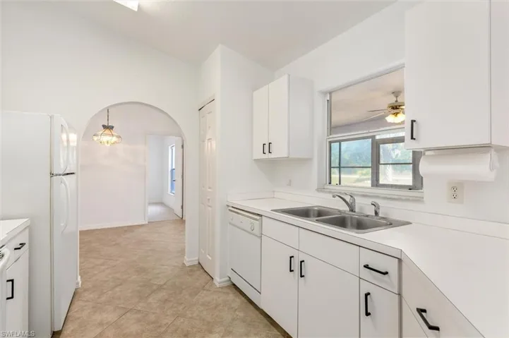 Kitchen featuring white cabinetry with black hardware, a double basin stainless steel sink, and light-toned countertops