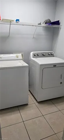 Washroom with light tile patterned floors, independent washer and dryer, and a textured wall