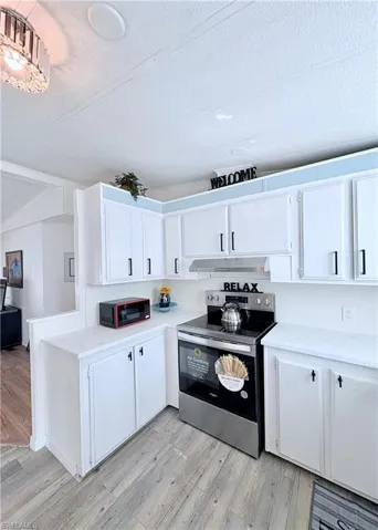 Kitchen featuring stainless steel range with electric stovetop, white cabinetry, a textured ceiling, black microwave, and light wood finished floors