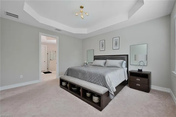 Bedroom with a tray ceiling, light carpet, and connected bathroom