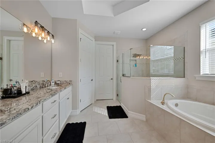 Full bath featuring vanity, a garden tub, light tile patterned flooring, a shower stall, and plenty of natural light