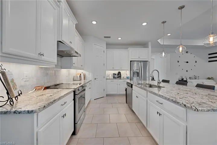 Kitchen with stainless steel appliances, white cabinetry, light stone countertops, pendant lighting, and a kitchen island with sink