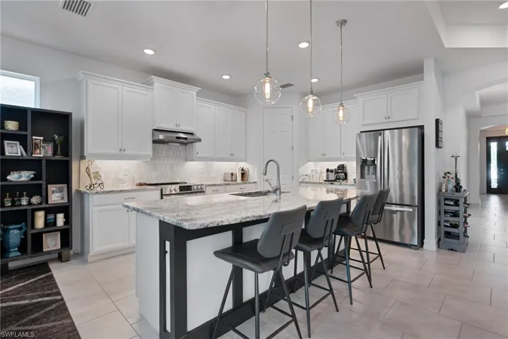 Kitchen with stainless steel appliances, arched walkways, light stone countertops, white cabinets, and a kitchen bar