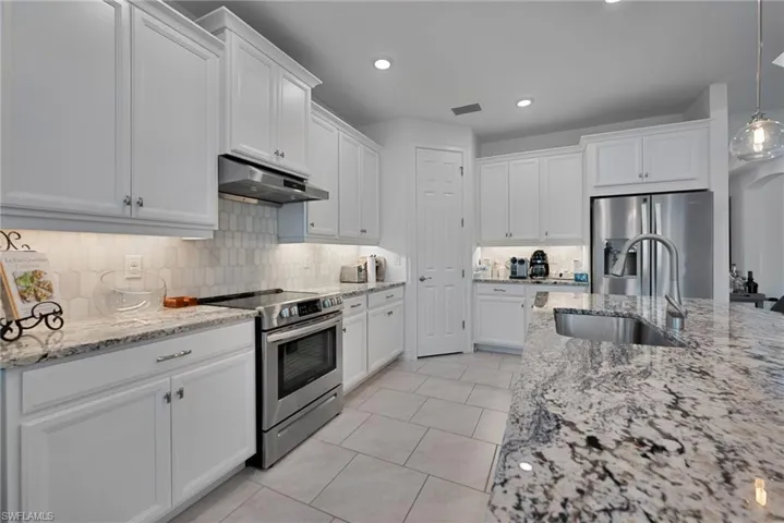 Kitchen with stainless steel appliances, light stone countertops, white cabinetry, pendant lighting, and tasteful backsplash