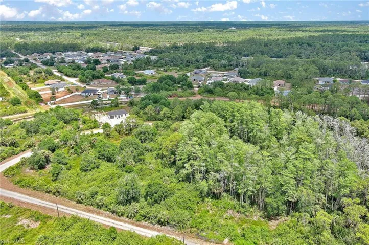 Aerial view of property and surrounding area featuring a heavily wooded area and nearby suburban area
