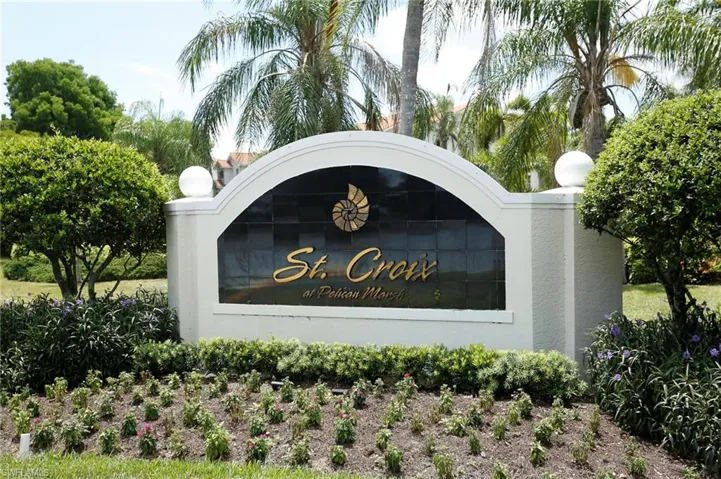 Community entrance signage featuring architectural detailing, lush landscaping, mature palm trees, and decorative globe lighting