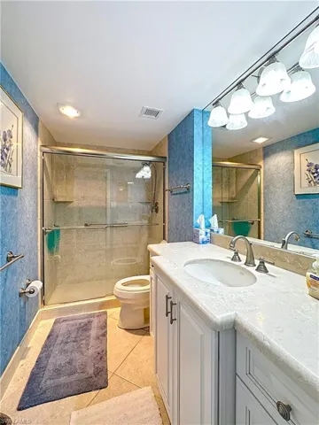 Full bathroom with wallpapered walls, tile patterned floors, toilet, vanity, and a stall shower