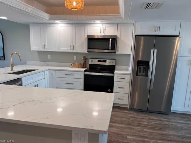Kitchen with stainless steel appliances, luxury vinyl tile flooring, white cabinets, and  light quartz countertops