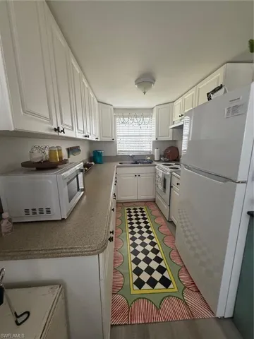 Kitchen with white cabinets, range, white refrigerator, range hood, and a sink
