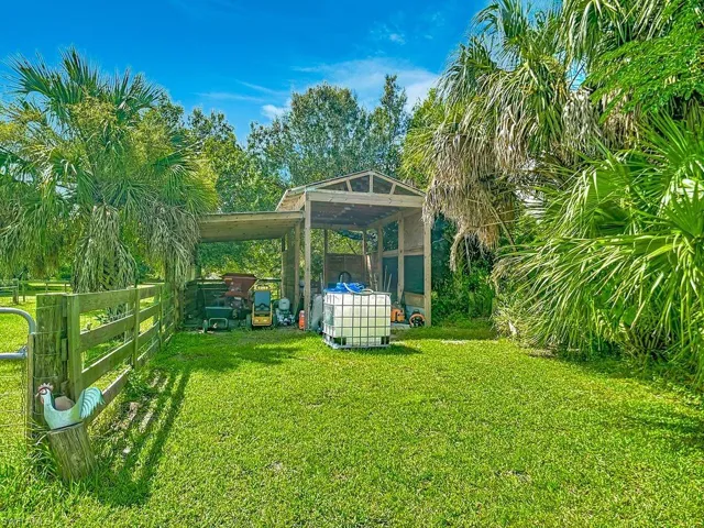Expansive green space featuring a wood-frame open-air structure, partial wood fencing, and mature palm trees