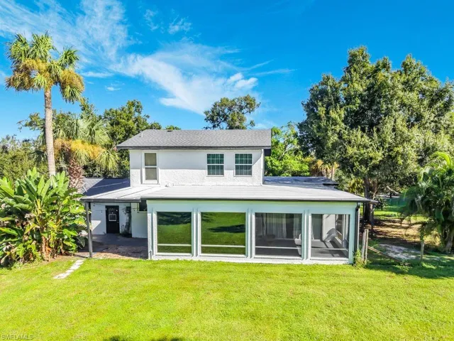 Expansive rear facade featuring a screened-in porch with multiple large windows, a well-maintained lawn, and mature landscaping