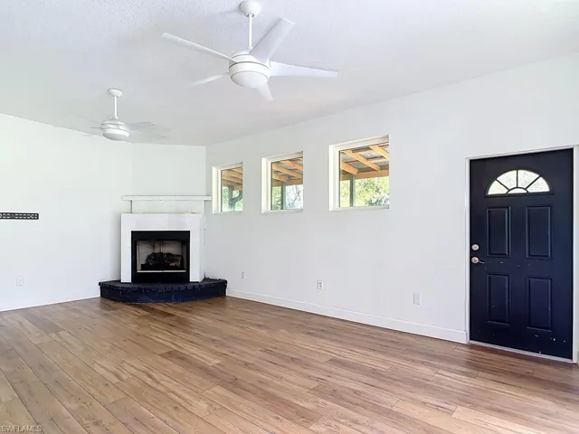 Wood-finish flooring, white walls, and a corner fireplace with a black hearth