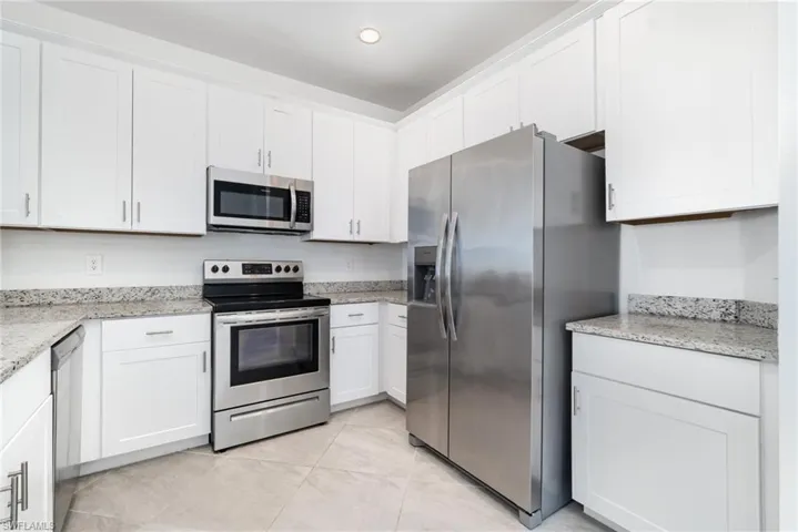Kitchen with appliances with stainless steel finishes, light stone countertops, white cabinetry, light tile patterned floors, and recessed lighting