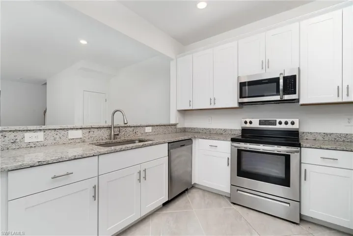 Kitchen featuring appliances with stainless steel finishes, light stone countertops, white cabinets, recessed lighting, and light tile patterned floors