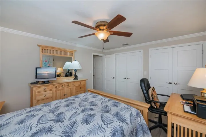 Bedroom with two closets, ornamental molding, a desk, and ceiling fan