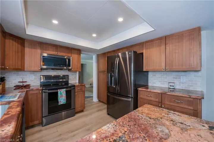 Remodeled kitchen featuring granite countertops, backsplash, stainless steel appliances, brown cabinetry, and recessed lighting!