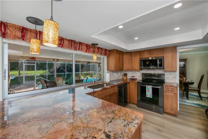 Kitchen featuring brown cabinets, stainless steel appliances, a tray ceiling, hanging light fixtures, and tasteful backsplash