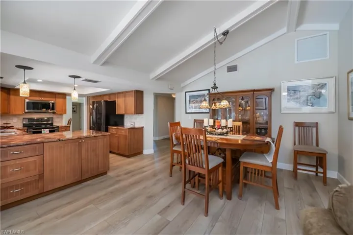 Dining area with beam ceiling, light wood-style floors, and high vaulted ceiling