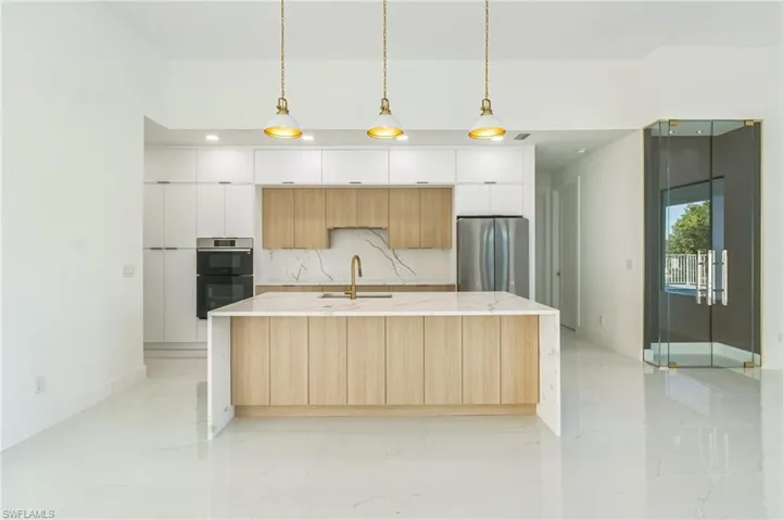 Kitchen with modern cabinets, a towering ceiling, stainless steel fridge with ice dispenser, white cabinets, and open floor plan