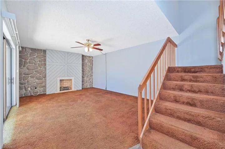 Unfurnished living room featuring a textured ceiling, carpet flooring, a ceiling fan, a fireplace, and an accent wall
