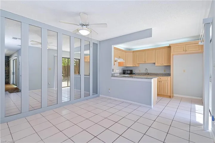 Kitchen featuring light wood finish cabinets, light tile patterned floors, a textured ceiling, light stone countertops, and black microwave