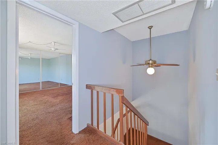 Hall featuring an upstairs landing, carpet, and a textured ceiling